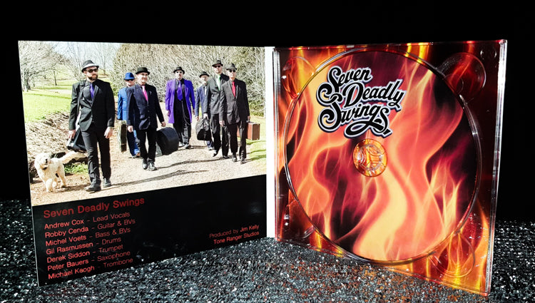 seven deadly swings album cover, artwork flames as background for title, insert showing band members carrying instrument cases along a road